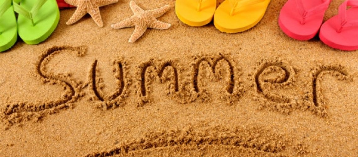 The word Summer written on a sandy beach, with beach towel, starfish and flip flops (studio shot - warm color and directional light are intentional).  Note: extreme wide angle shot with curvature of field and focus on the word Summer.